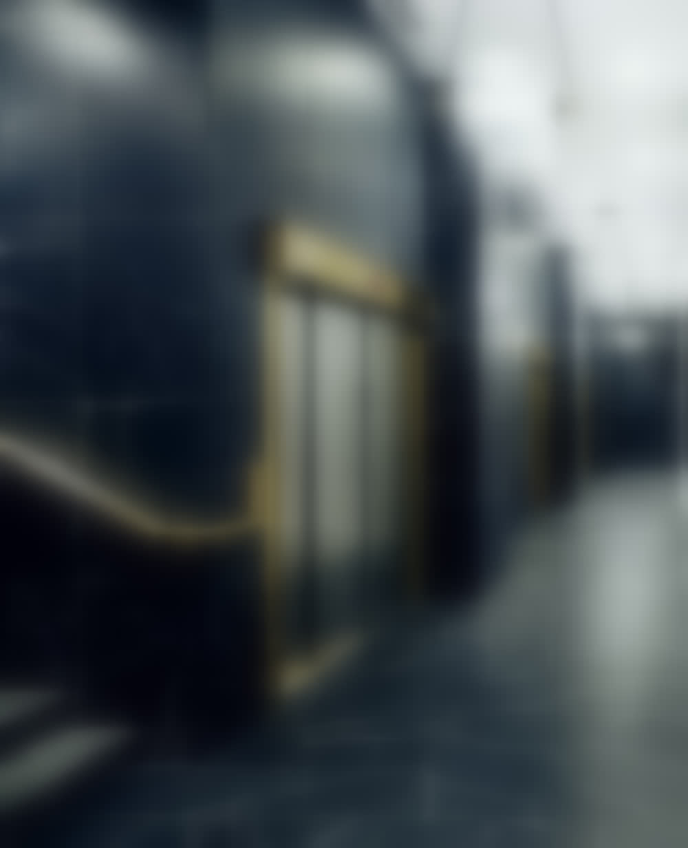 The lift bay at 63-67 Wall Street: black veined marble, a brass-framed door and handrail, a glass globe pendant above.