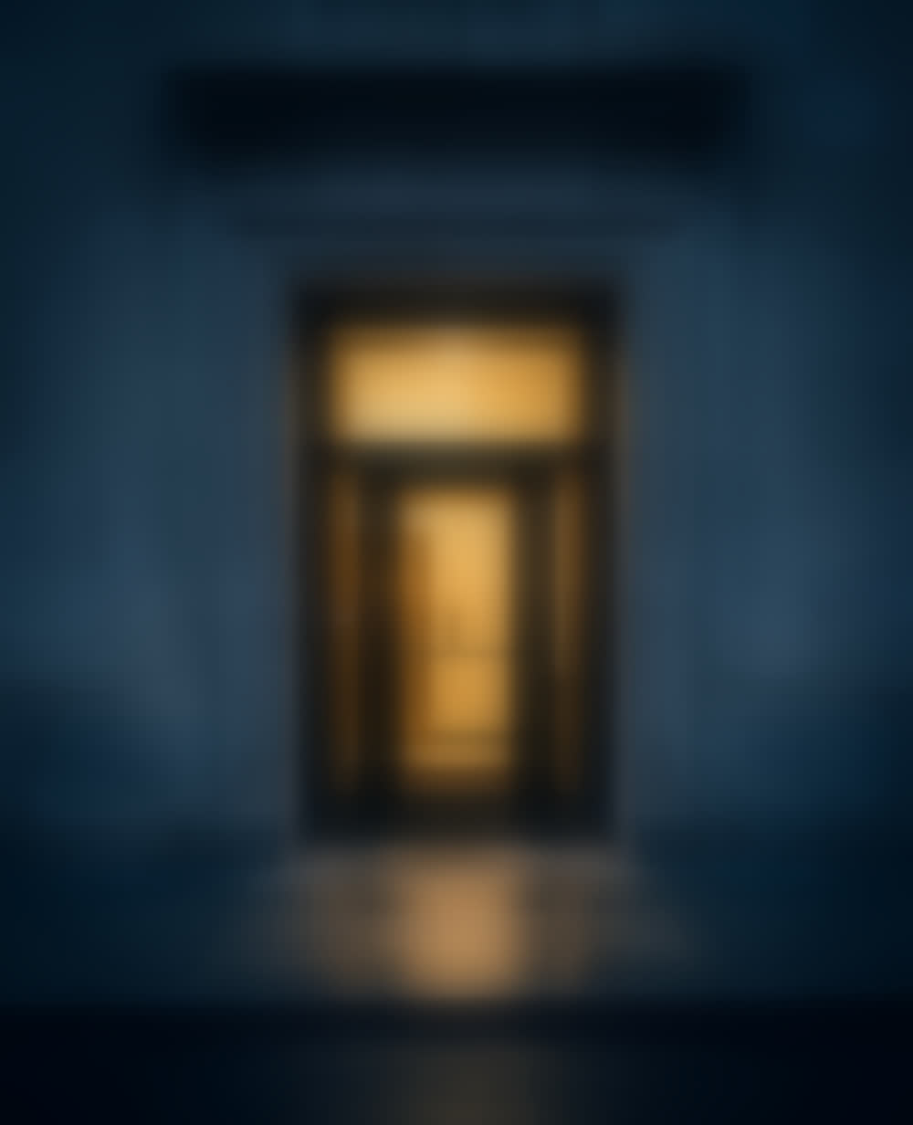 A lit doorway in a Financial District facade at dusk, the lobby glowing through the glass.