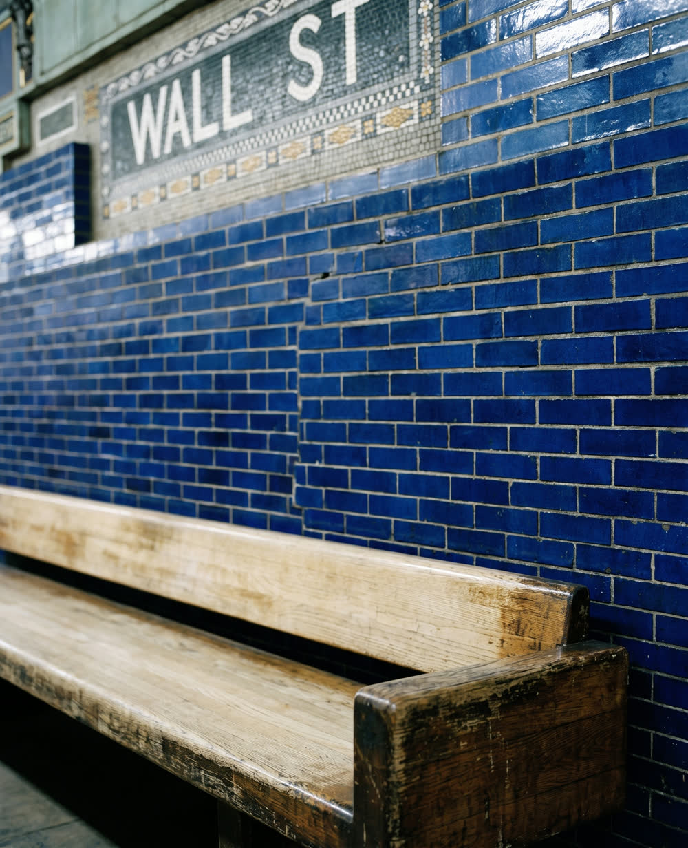 A worn oak bench against the cobalt tiled wall of the Wall Street subway station.