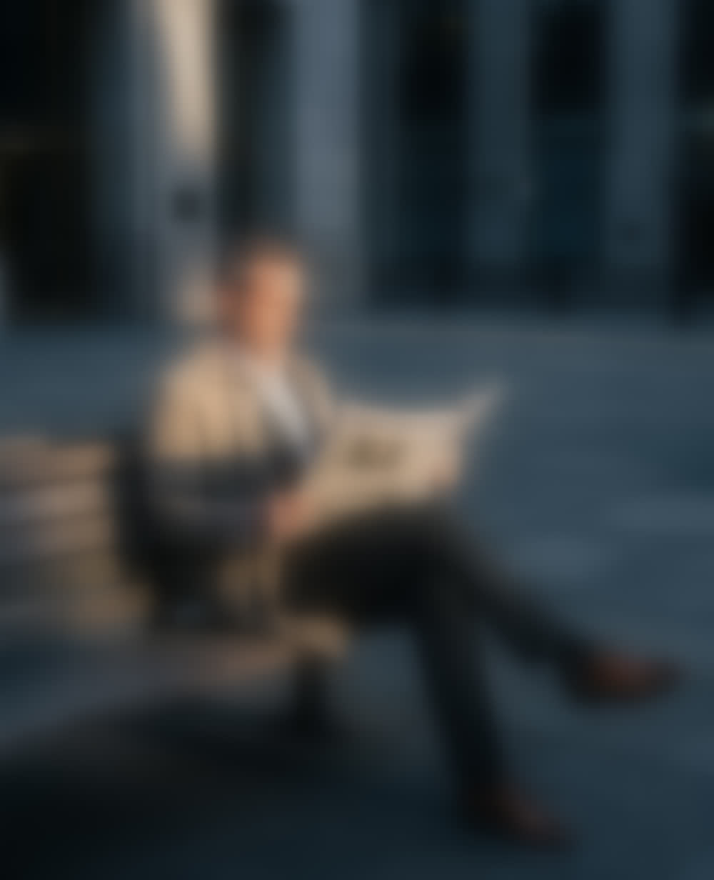 A man in a trench coat reading The Wall Street Journal on a bench in the Financial District.