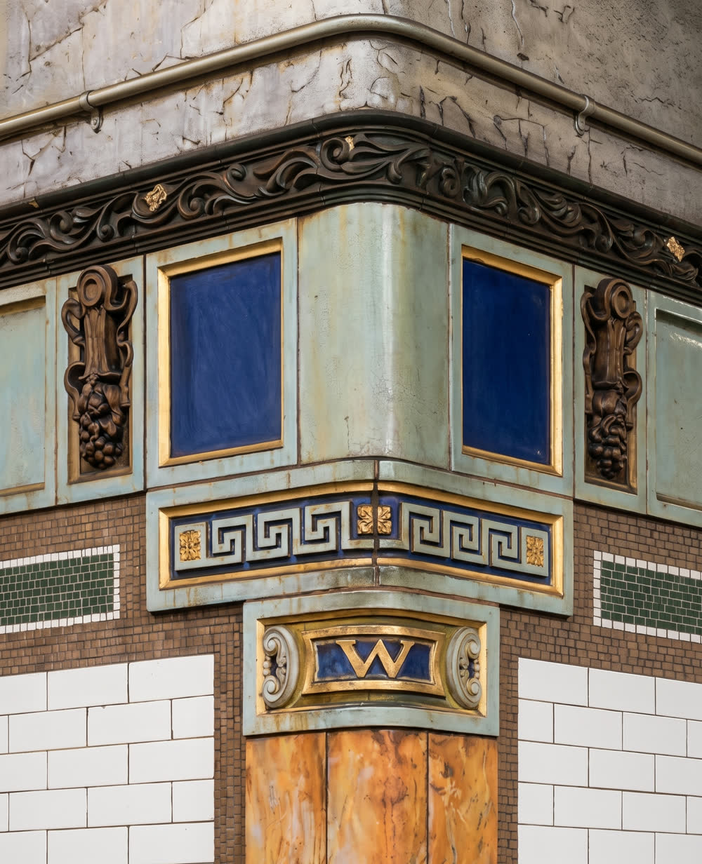 The ornamental faience corner pilaster at Wall Street subway station, with its gilt W cartouche.